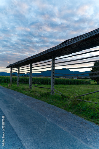 Hayrack at farmland between villages of Zabnica and Sutna with corn field and houses in the background on a blue cloudy summer evening. Photo taken August 10th, 2023, Zabnica, Kranj, Slovenia. © Michael Derrer Fuchs