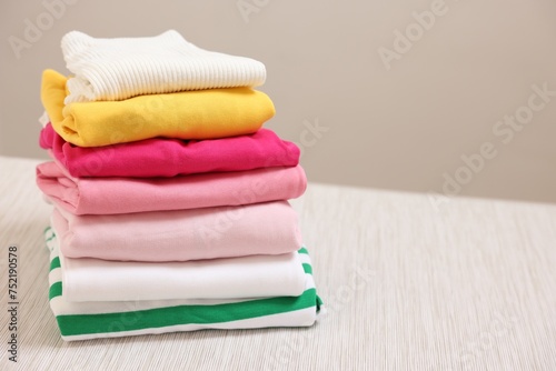 Stack of folded clothes on wooden table against beige background, space for text