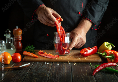 The chef preserves peppers with aromatic spices in a jar in the kitchen. Low key concept for preparing a canned vegetable dish. photo