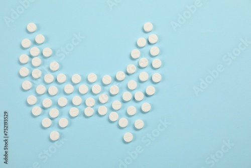 Endocrinology, Shape of thyroid gland made of pills on light blue background, flat lay. Space for text