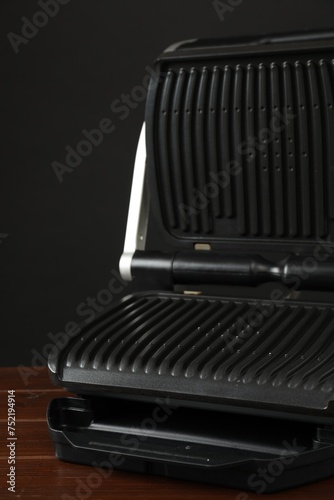 Electric grill on wooden table against black background, closeup. Cooking appliance