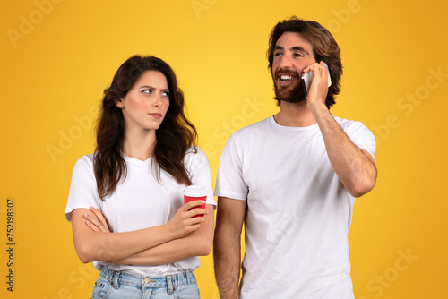 A skeptical woman holding a coffee cup looks askance at a cheerful man talking on a mobile phone photo