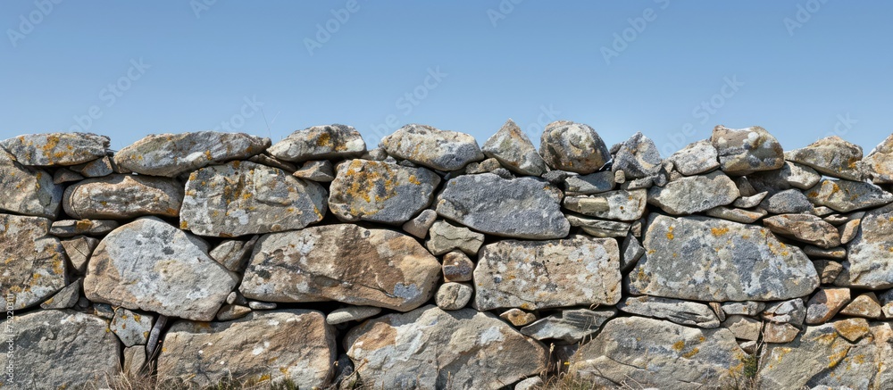 A weathered stone wall made of rocks with a backdrop of a clear blue sky in the background. A weathered stone wall made of rocks with a backdrop of a clear blue sky in the background.