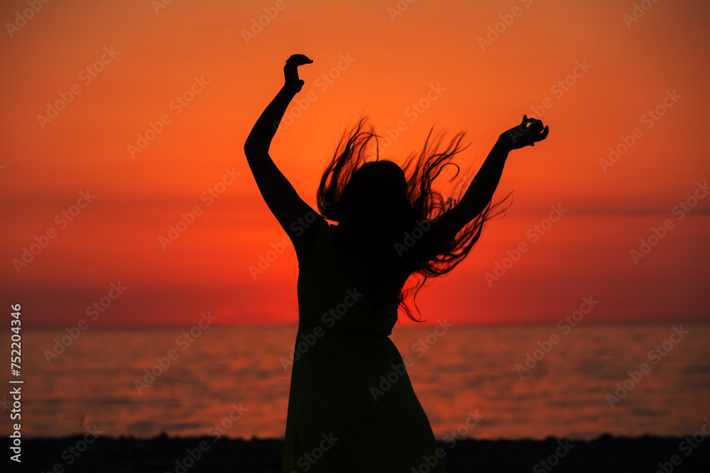 The silhouette of a woman with long hair against the background of the setting sun over the sea.