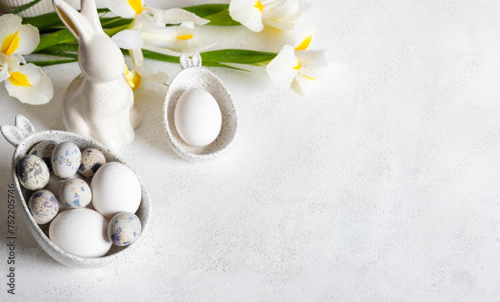 Fototapeta premium Easter white holiday card. Natural colors eggs in figured bowls, ceramic bunny, flowers. Copy space.