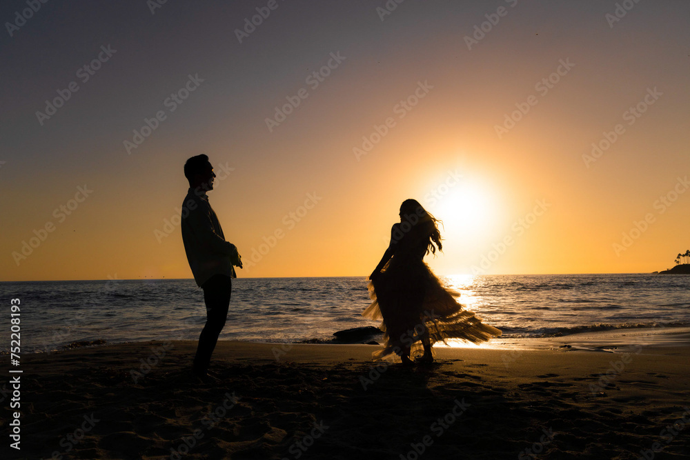 Silhouetted bride and groom against the sun with a water background.
