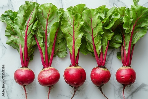 Fresh beetroots with vibrant green leaves and red stems on a marble background. Flat lay composition with copy space. Healthy eating and organic farming concept. 