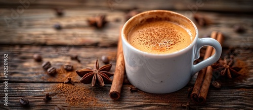A cup of coffee surrounded by cinnamons and star anise on a weathered wood surface.