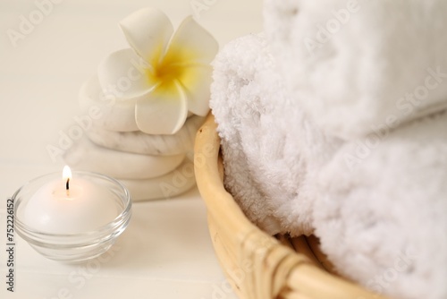 Spa composition. Rolled towels, massage stones, burning candle and plumeria flower on table, closeup
