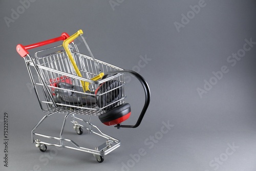 Small shopping cart with hacksaw, gloves and headphones on grey background. Space for text