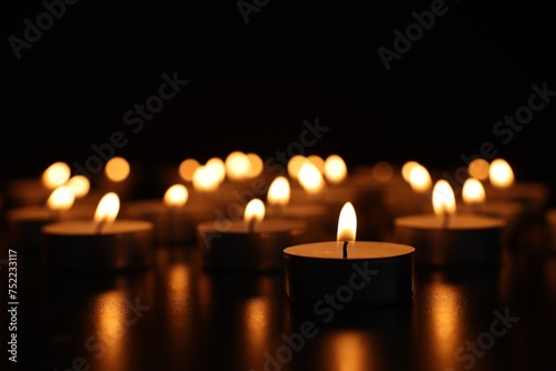 Burning candles on dark surface against black background, closeup