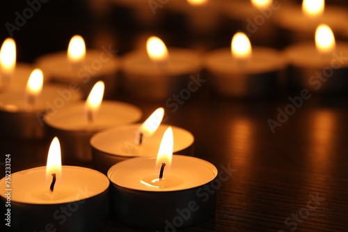 Burning tealight candles on dark surface  closeup