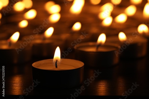 Burning candles on wooden table in darkness  closeup