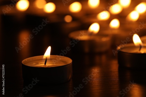 Burning candles on table in darkness, closeup. Space for text