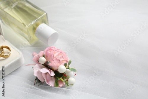 Wedding stuff. Stylish boutonniere  wedding rings and perfume bottle on white veil  closeup pace for text