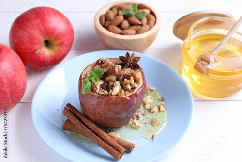 Tasty baked apple with nuts, honey, spices and mint on white wooden table, closeup