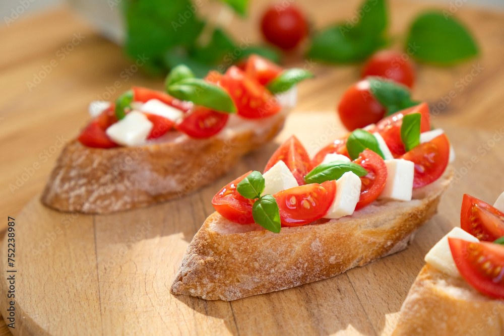 Caprese bruschetta with tomatoes, mozzarella cheese and basil in sun rays on wooden board. Traditional Italian appetizer, snack or antipasto. Vegetarian food. Healthy eating. Mediterranean food.