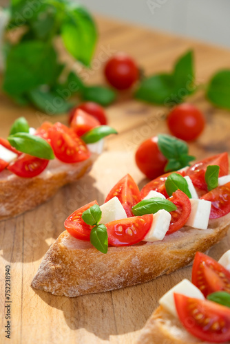 Caprese bruschetta with tomatoes, mozzarella cheese and basil in sun rays on wooden board. Traditional Italian appetizer, snack or antipasto. Vegetarian food. Healthy eating. Mediterranean food.