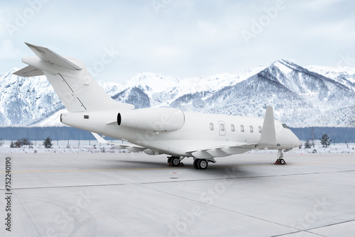 Modern white private jet at the airport apron on the background of high scenic snow capped mountains