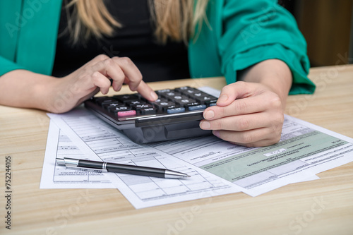 Kobieta pracuje przy biurku wypełnia dokumenty i liczy na kalkulatorze 