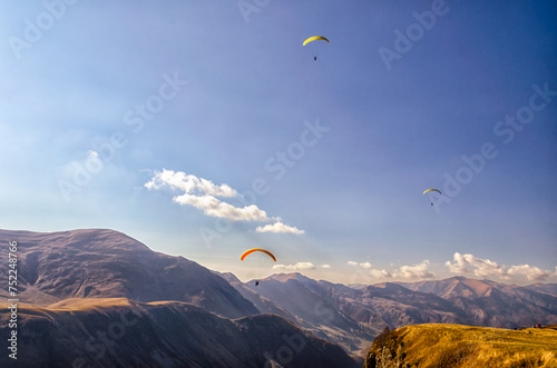 three paragliders in sky against the background of Caucasus mountains