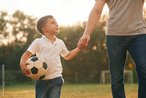 Walking and holding soccer ball. Father and little son are playing and having fun outdoors © standret