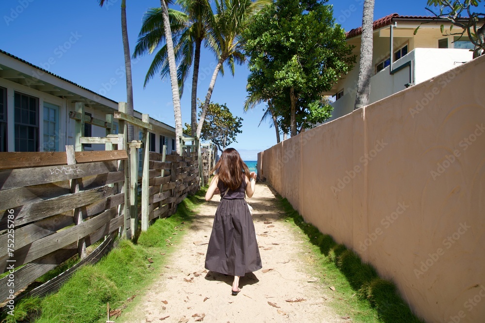 Woman walking on a narrow sandy path leading to Lanikai Beach, Hawaii.