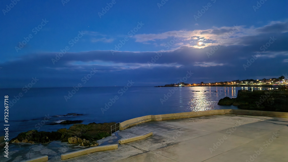Dún Laoghaire by Night: A luminous spectacle, the town sparkles with lights, casting a magical glow over the tranquil waters, creating a captivating nocturnal panorama.