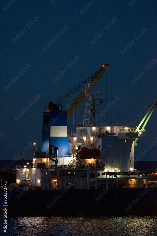 Nocturna vertical barco carga en puerto, iluminado