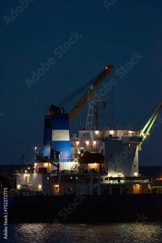 Nocturna vertical barco carga en puerto, iluminado
