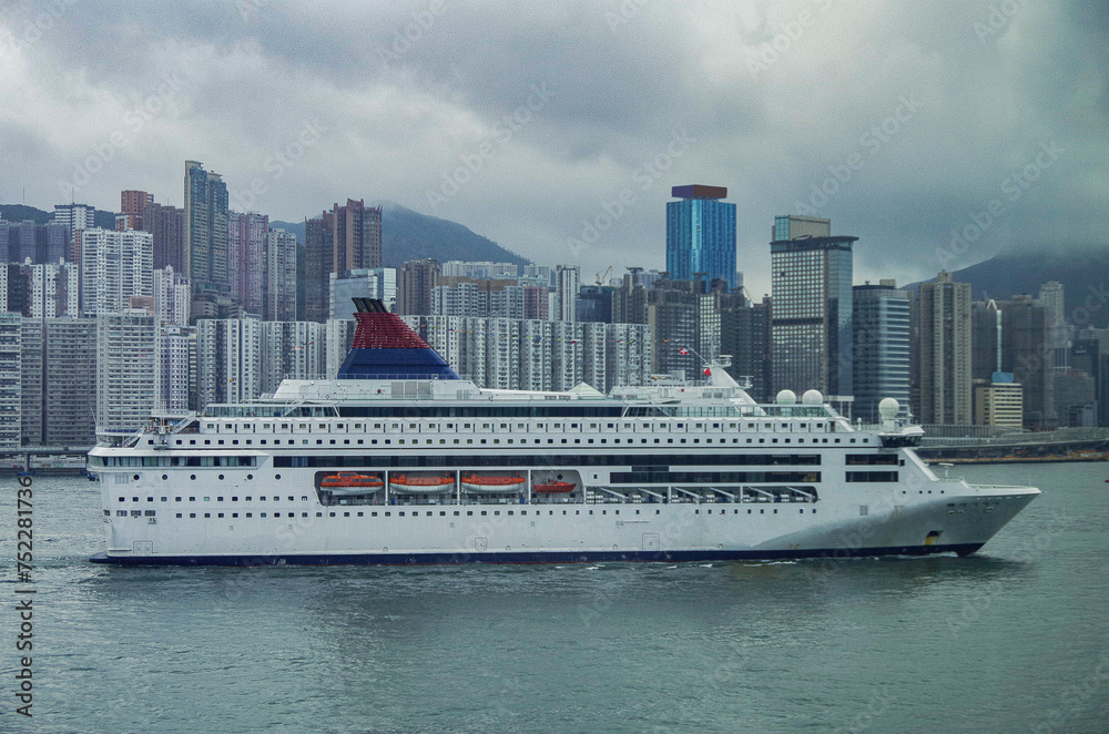 Classic cruiseship cruise ship liner Pisces arrival into Victoria Harbor in Hong Kong Honkong, China on grey cloudy day with city skyline Classic cruiseship cruise ship liner Pisces arrival into Victoria Harbor in Hong Kong Honkong, China on grey cloudy day with city skyline