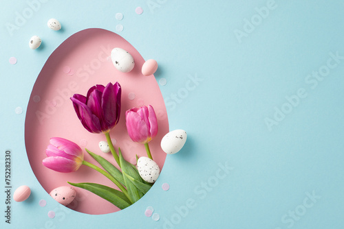 Lovely Easter composition captured from the top, with vibrant tulips and Easter eggs visible through a pink egg-shaped hole on a soft blue background, leaving space for text or adverts photo