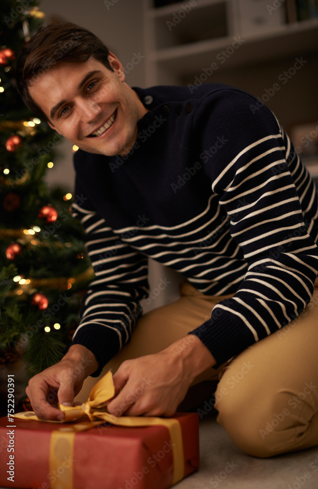 Portrait, Christmas tree and man wrapping gift in home for preparation of holiday event of tradition. Gift, present and smile with happy young person in apartment for December celebration or vacation