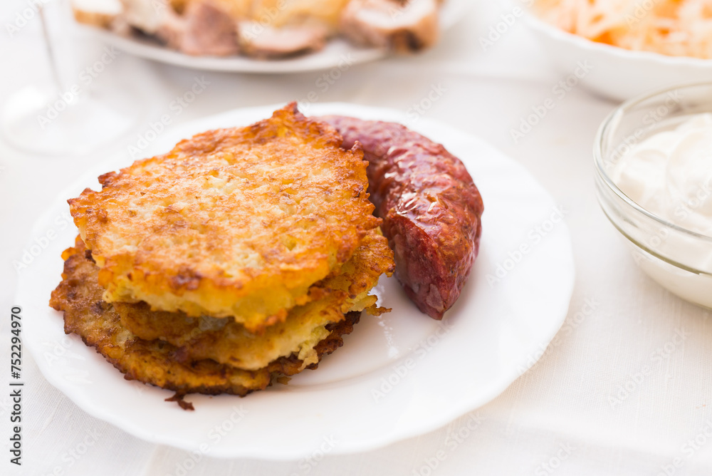 Fried grated potato pancakes with fried sausage on white plate