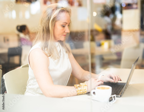 Business woman drinks coffee and works on laptop while sitting at table in cafe