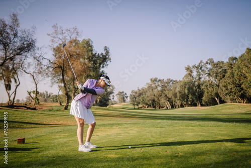 Agadir, Morocco - February 25, 2024 - A woman in a purple top and white skirt is in mid-swing playing golf on a sunny day