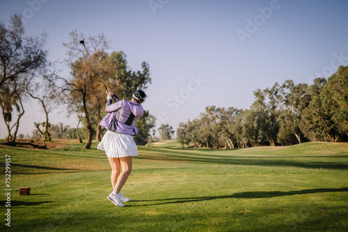 Agadir, Morocco - February 25, 2024 - A golfer in a purple top and white skirt finishes her swing on a sunny golf course...