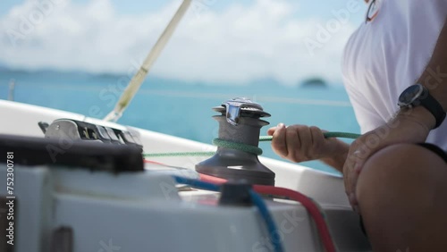 Sailor's hand on a winch of sailing boat. Close Up of Sailman Hands Unwinding Rope From Winch of Sailboat on Sunny photo