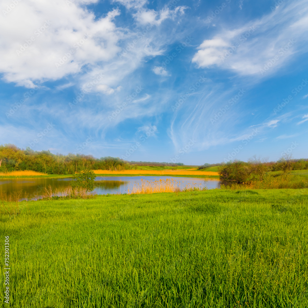 Obraz premium small lake among green hills at calm bright spring day, seasonal countryside landscape