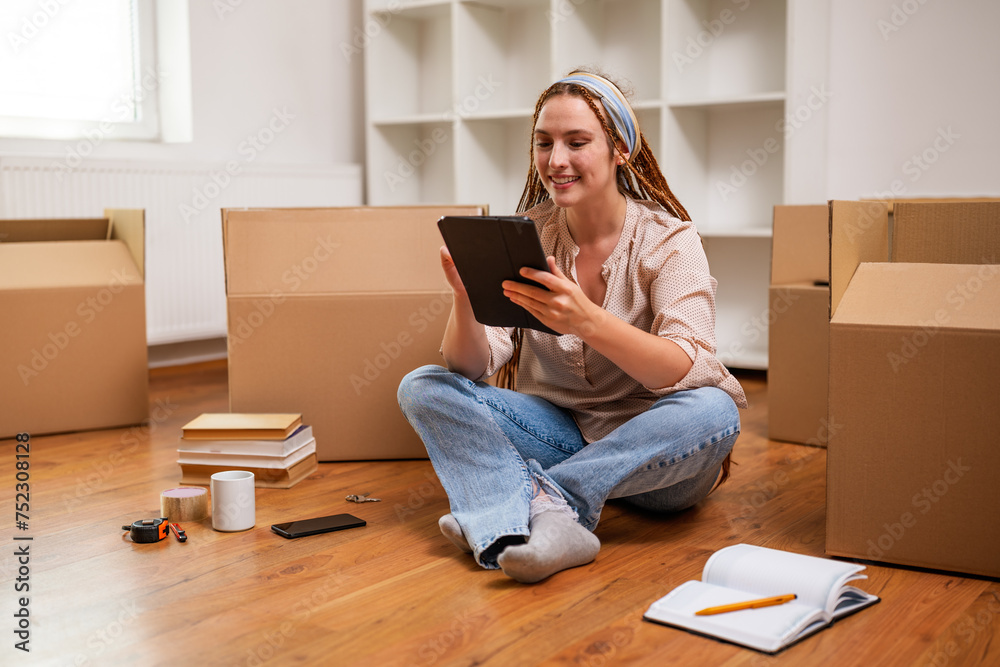Modern ginger woman with braids using digital tablet while moving into new apartment. Modern ginger woman with braids using digital tablet while moving into new apartment.