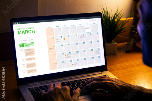 Monthly planner schedule. Man looking at digital calendar on laptop screen, at night to plan the next day.