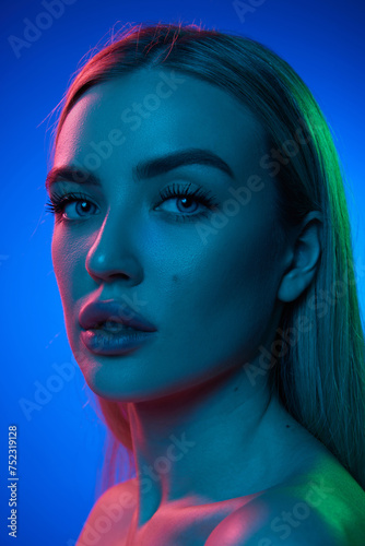 Portrait of attractive young woman with perfect, spotless skin posing against blue studio background in neon light. Concept of natural beauty, cosmetology, cosmetics, skin care and health