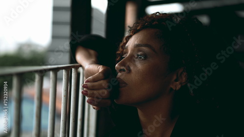 One sad pensive black middle-aged woman gazing at view from balcony in deep melancholic contemplation. Close-up face of an African American lady feeling lost in thought, pondering life's challenges photo