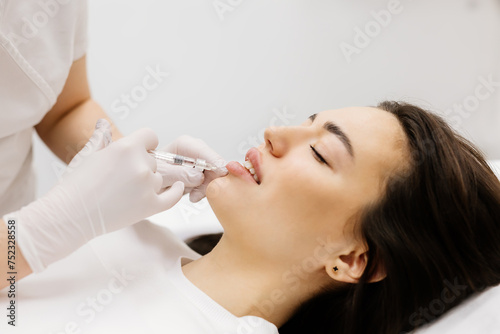 Injection lip augmentation. Close-up of beautician s hands doing cosmetic procedures for sexy female lips. Cosmetological treatment  cosmetic injections.