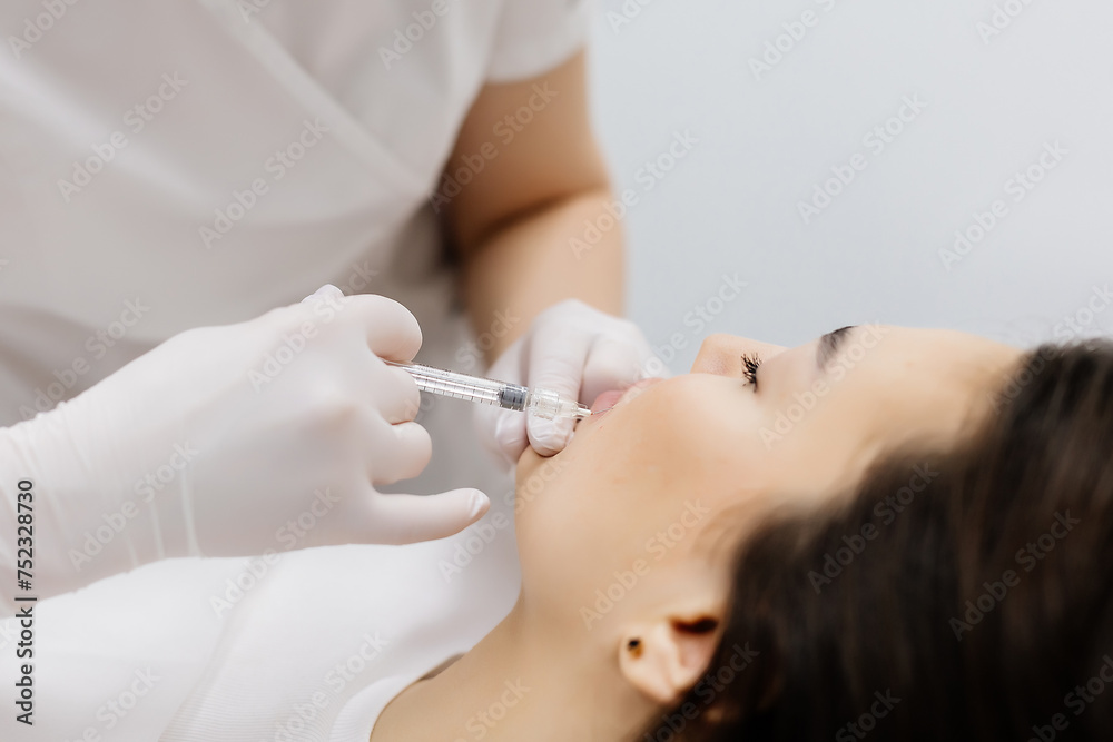 Injection lip augmentation. Close-up of beautician's hands doing cosmetic procedures for sexy female lips. Cosmetological treatment, cosmetic injections.
