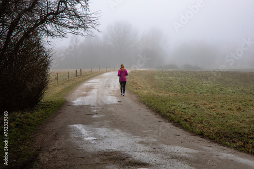 Natural landscape of a foggy morning in the countryside and an athletic woman runs along the road in sportswear. Foggy farm field.