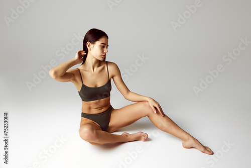 Self-love. Young attractive, slim woman sitting, posing on floor in chocolate underwear against grey studio background. Concept of beauty, spa procedures, dermatology treatments, cosmetology care.