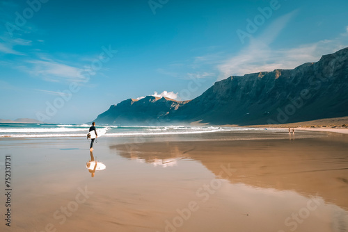 surfista si specchia su spiaggia in riva all'oceano sotto la scogliera photo