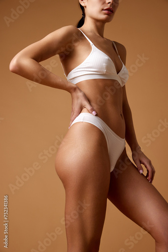 Fit and healthy. Young, slim woman in white lingerie with well-kept, smooth skin against sandy color studio background. Concept of beauty, spa procedures, dermatology treatments, cosmetology care.
