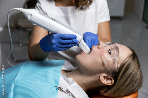 Orthodontist using a digital scanner to digitally capture the shape of blonde caucasian woman patient teeth gums for custom made invisible plastic aligners bracers. Quick oral scanning by the doctor